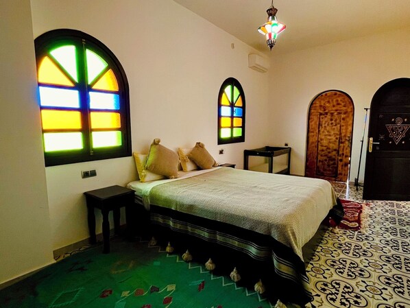 A room with a bed, a small table, a decorative mirror, and a door with a geometric design.