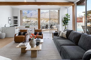 A modern living room with a sofa, chairs, a coffee table, and a view of mountains through large windows.