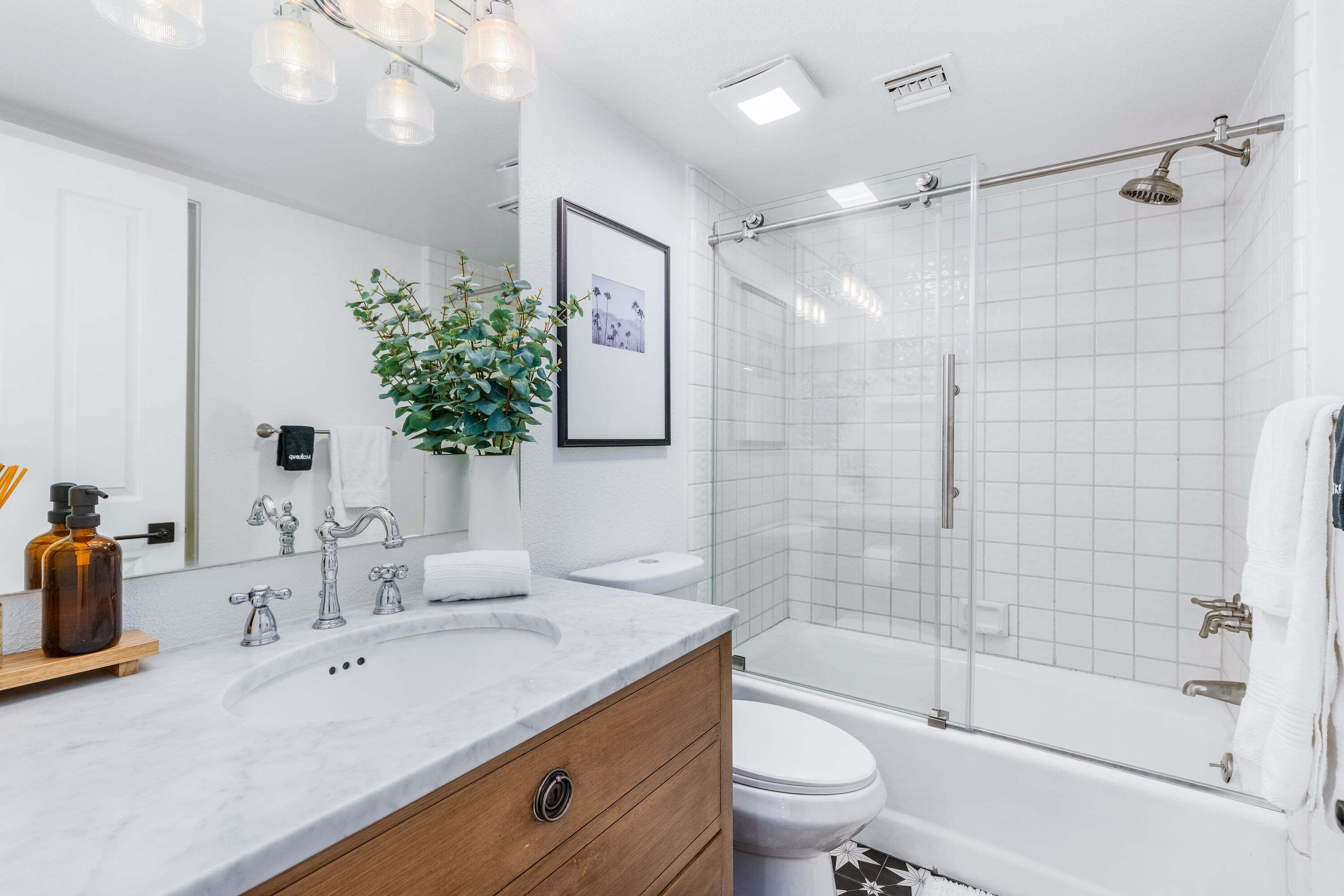 Ein modernes Badezimmer mit Marmorwaschbecken, Toilette, einer Duschkabine aus Glas und einem gerahmten Bild an der Wand.