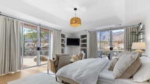 Un dormitorio con cama, televisor, sillón y vista al exterior.
