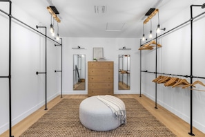 A walk-in closet with a round ottoman, wooden dresser, and mirrored closet doors.