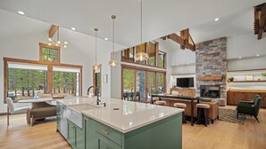 Une cuisine spacieuse dotée d’un grand îlot central, de poutres en bois et de grandes fenêtres offrant une vue sur l’extérieur.
