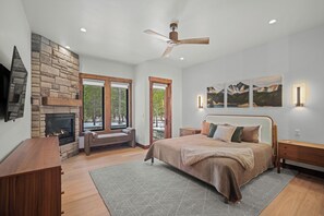A spacious bedroom with a stone fireplace, a large bed with multiple pillows, a wooden nightstand, a desk, and a ceiling fan. - Luxe Caldera Lodge with Access to Forest House (Sunriver)