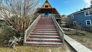 Una casa con una escalera pronunciada que lleva a la puerta principal, rodeada de árboles y un cielo azul claro.