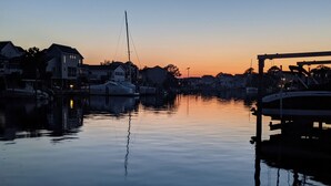 Una marina con agua tranquila que refleja el atardecer, barcos amarrados y edificios residenciales al fondo.