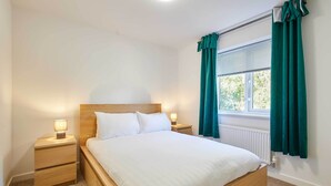 Un letto rifatto con cura in una stanza con una testiera in legno, un comodino con una lampada e una finestra con tende.