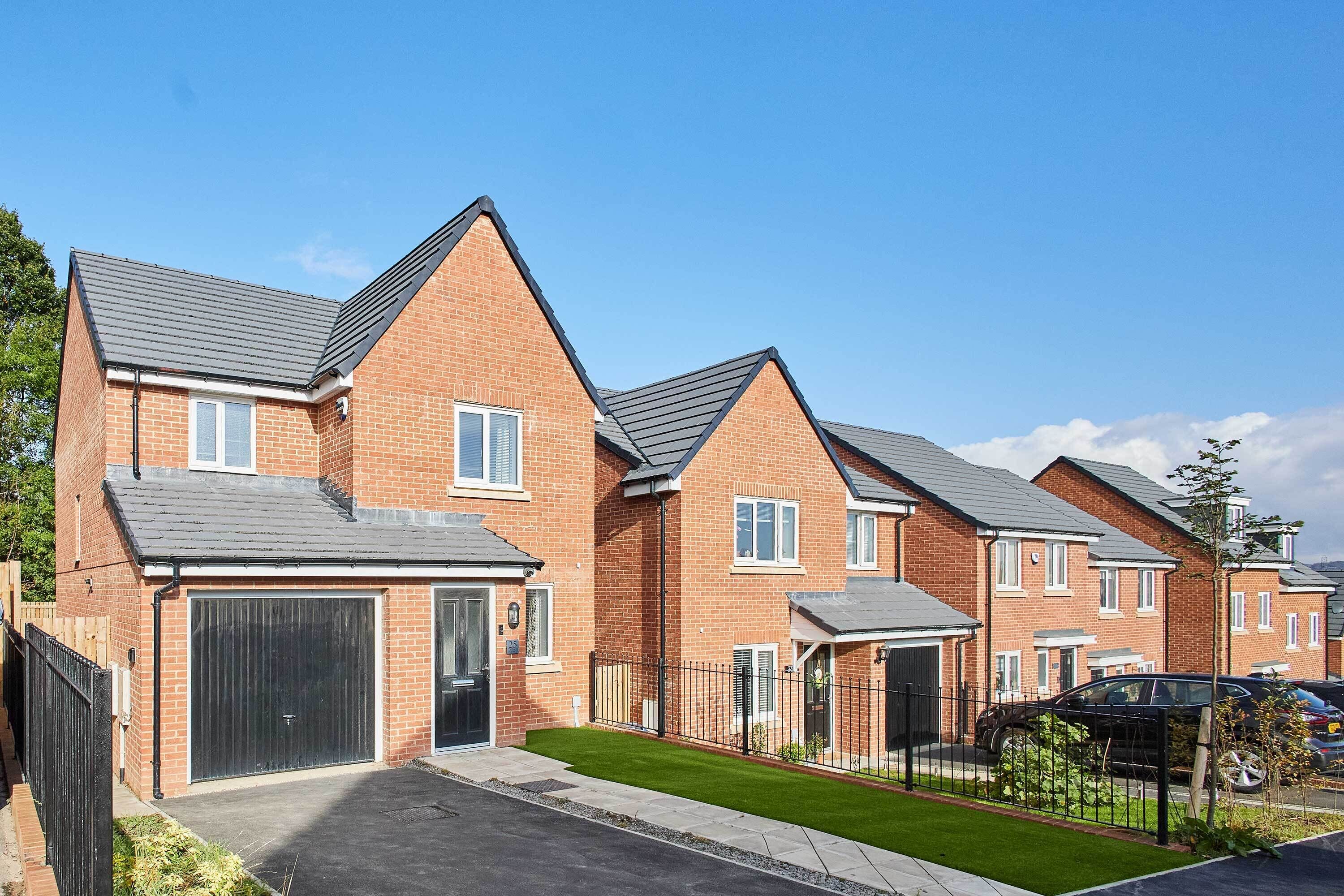 Une rangée de maisons modernes en briques, dotées de garages attenants et d’une pelouse bien entretenue.
