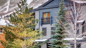 A two-story building with a balcony, surrounded by trees and a snowy mountain backdrop.