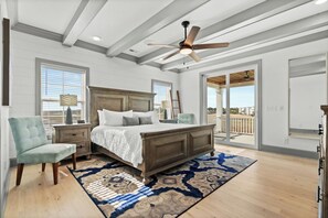 A bedroom with a large bed, a ceiling fan, a view through the door, and a wooden floor.