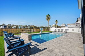 A swimming pool with lounge chairs and a basketball hoop, surrounded by a fence and palm trees.