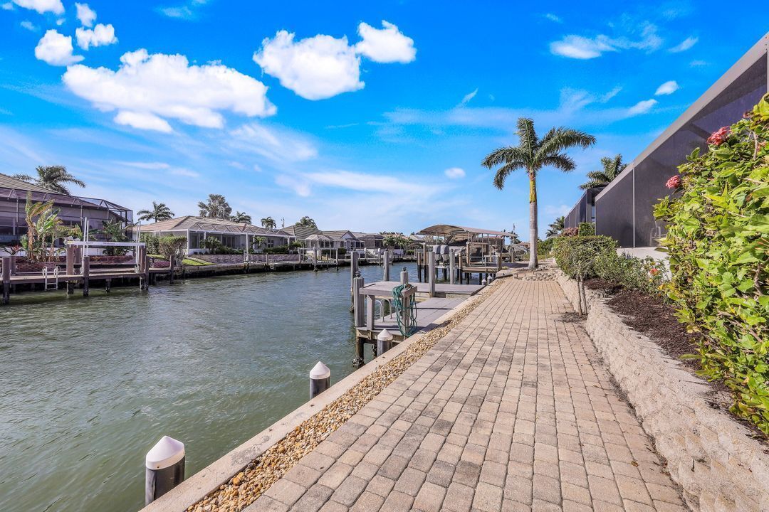 A waterfront hotel with a paved walkway, docked boats, and palm trees.
