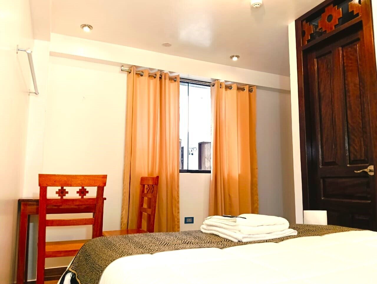 Une chambre d’hôtel avec un lit, une chaise, une fenêtre avec des rideaux et une porte.