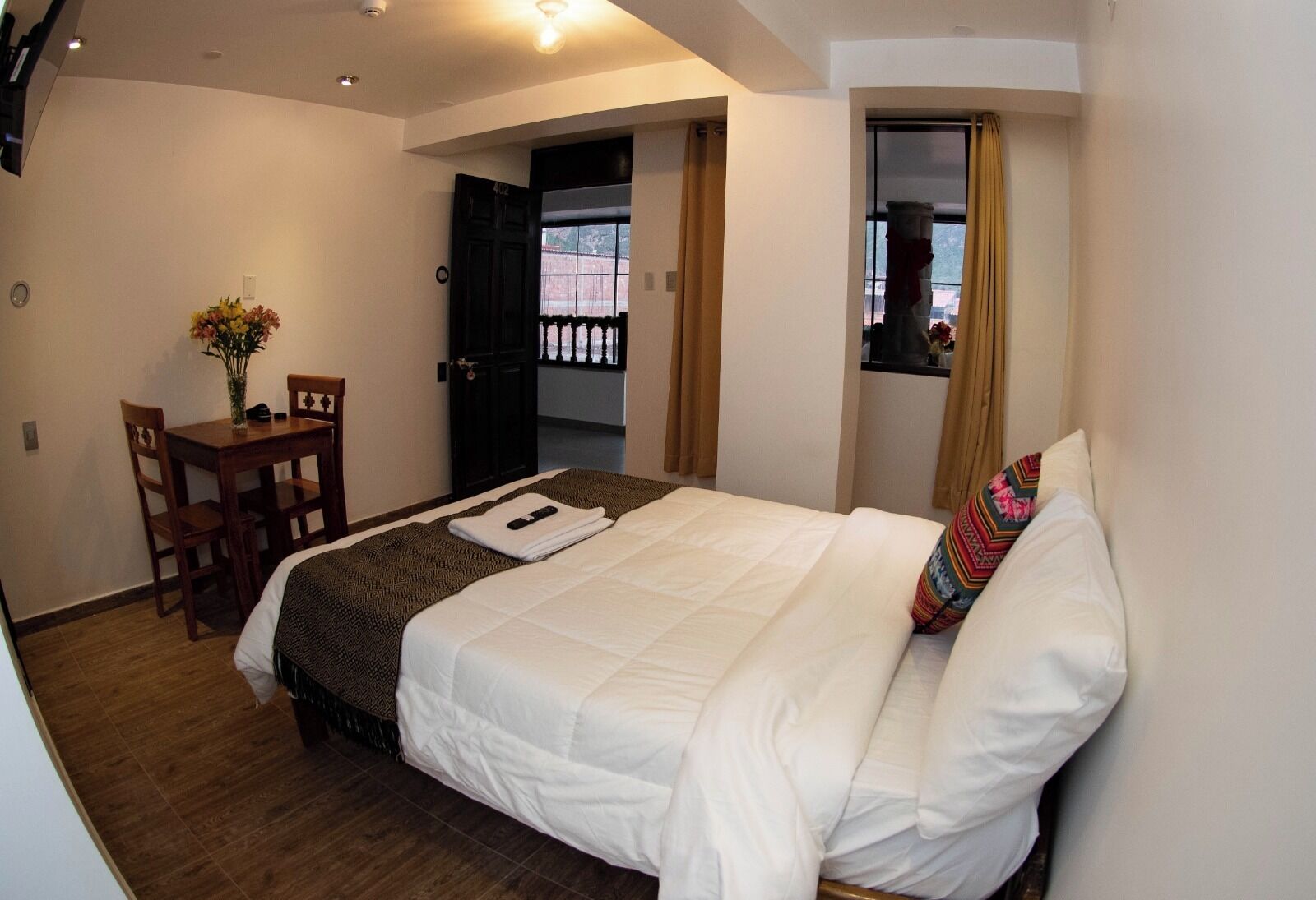 Une chambre d’hôtel avec un lit, un bureau et une chaise, un vase avec des fleurs et une fenêtre avec des rideaux.