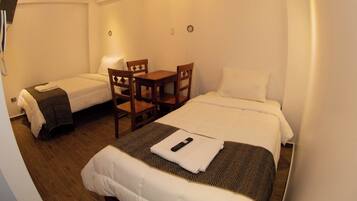 A hotel room with two single beds, a wooden table, and a small desk.