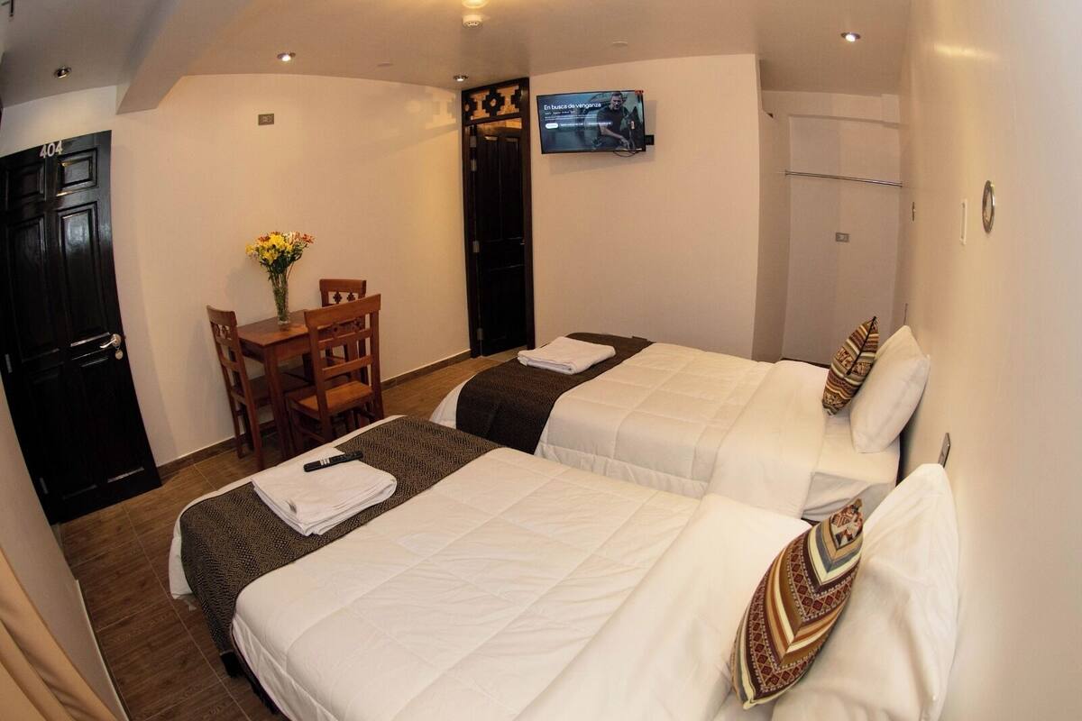 A hotel room with two beds, a TV mounted on the wall, a desk with a chair, and a door labeled 404.