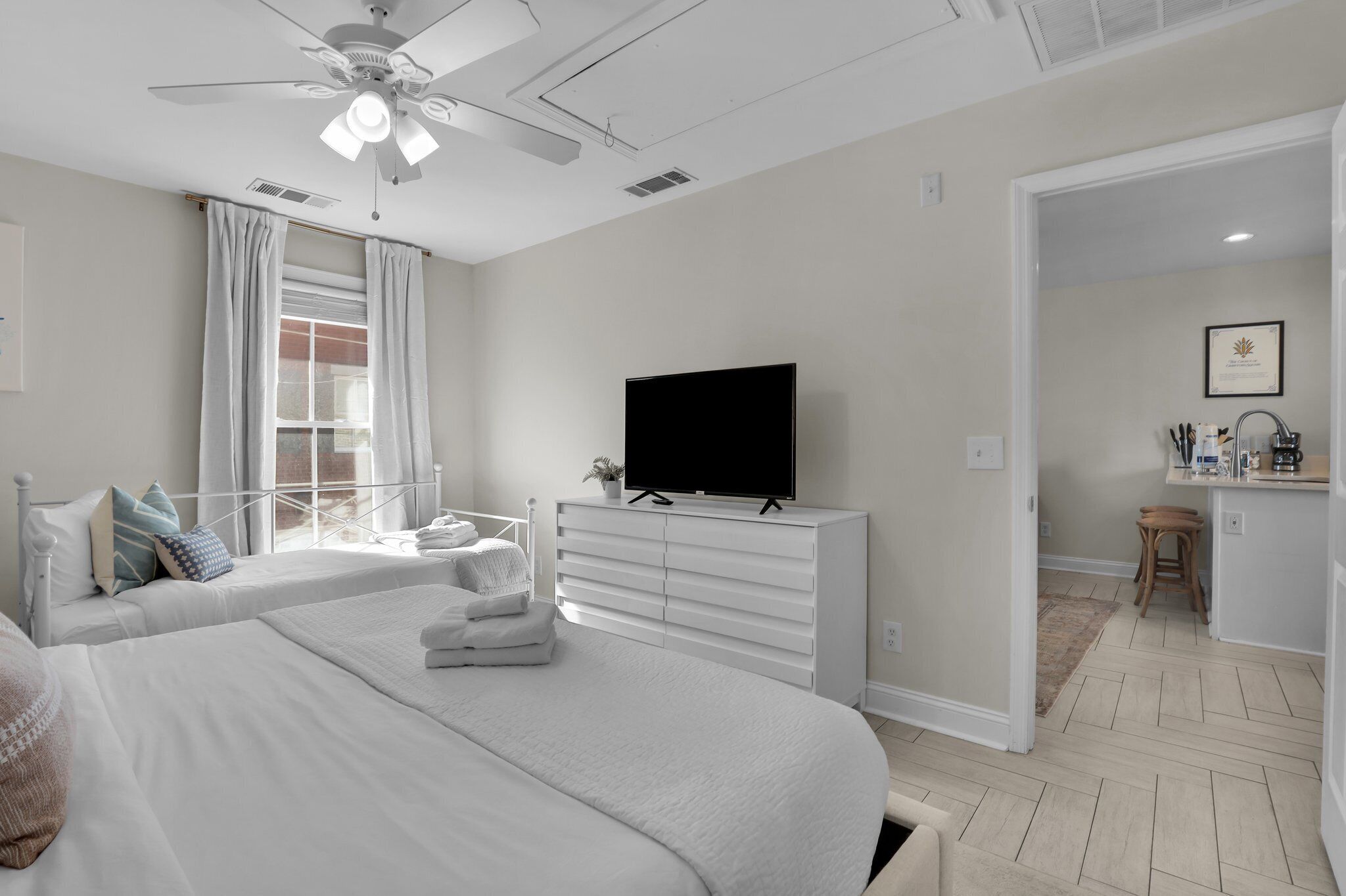 A bedroom with a bed, a TV, a ceiling fan, and a window with curtains.