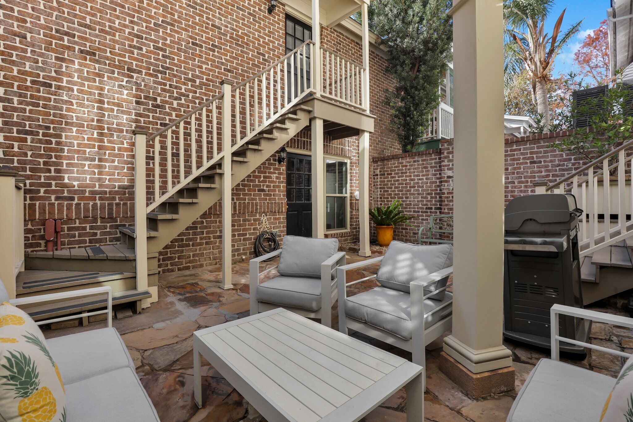 A patio with outdoor furniture, a brick wall, and a staircase leading to a second floor.