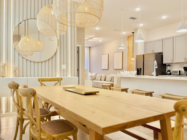 A modern kitchen with white cabinets, a stainless steel refrigerator, and a wooden dining table with chairs. - Pvt Pool, BBQ & Club Access Spacious 5-Bed Home in Int’l Drive Orlando (Orlando)