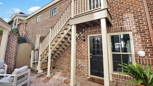 A brick building with a staircase leading to a second floor, a front door, and a small patio area with outdoor furniture.