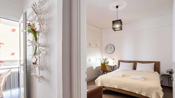 A bedroom with a bed, a bedside table, a chair, a desk, and a wall-mounted clock. - Elena's Cozy & Central Nest (Kalamata)