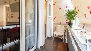A balcony with a wicker chair, a potted plant, and a view of the interior. - Elena's Cozy & Central Nest (Kalamata)