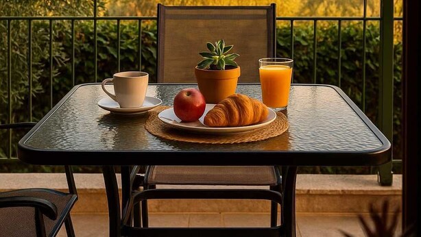 A table set with a croissant, apple, coffee cup, and orange juice on a balcony with a view of trees and mountains. - Aelia Guesthouse - Private Garden Retreat (Daras)