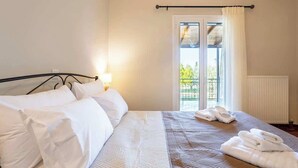 A neatly made bed with white linens, a bedside lamp, and a view of a balcony through a window with white curtains. - Aelia Guesthouse - Private Garden Retreat (Daras)