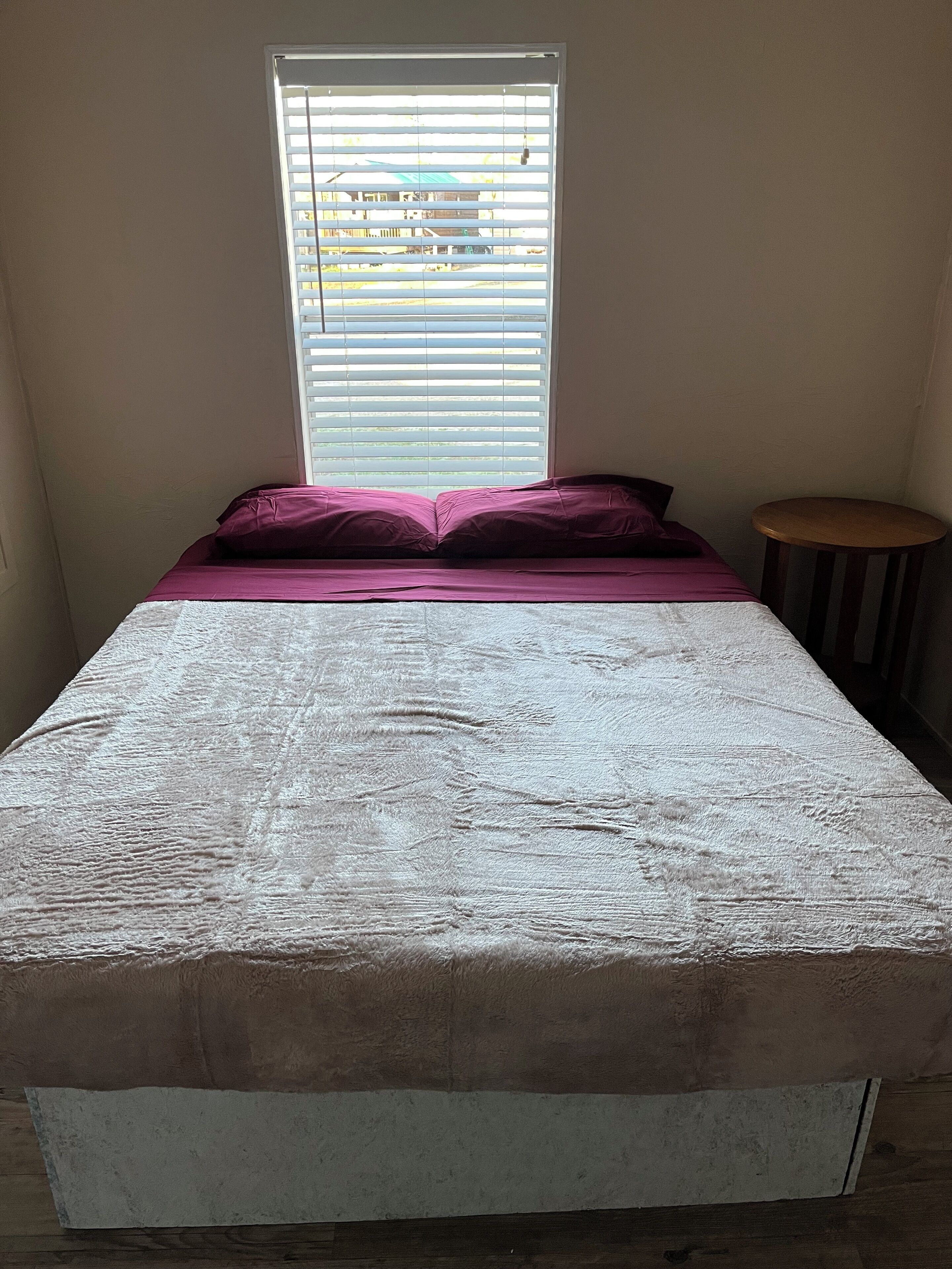A small, single-bed room with a window and a small wooden stool.