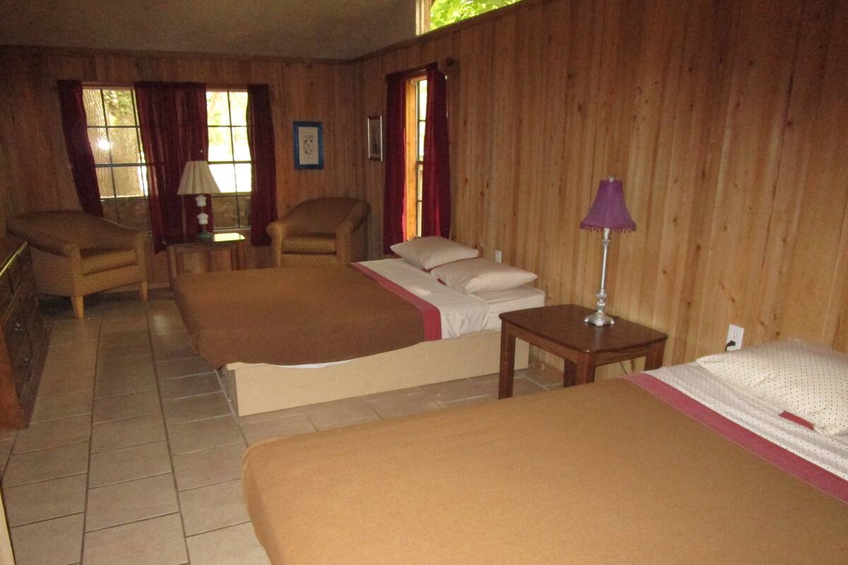 A room with two beds, a chair, a table, and a window.