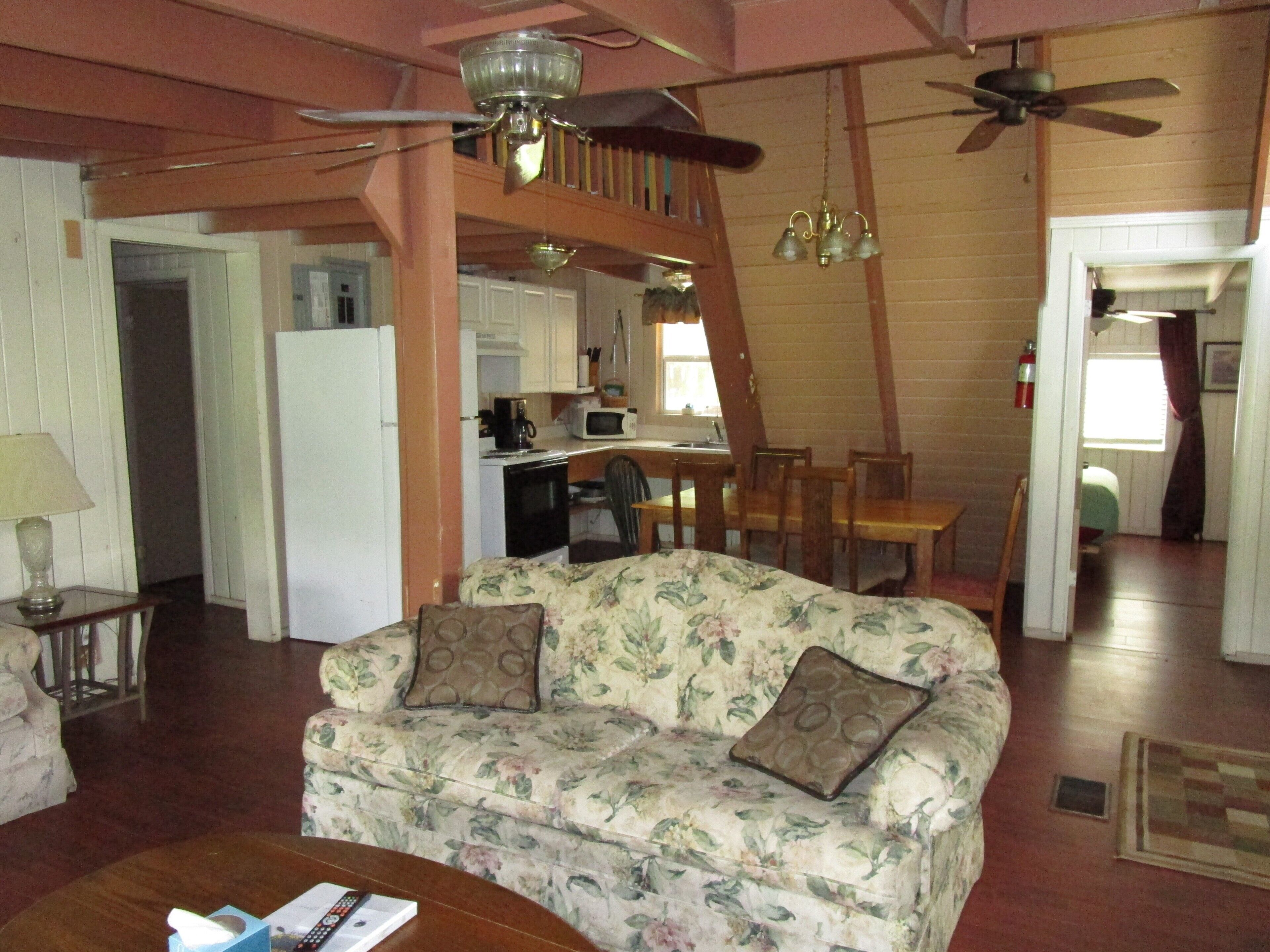 A cozy living room with a floral sofa, a wooden coffee table, and a ceiling fan.
