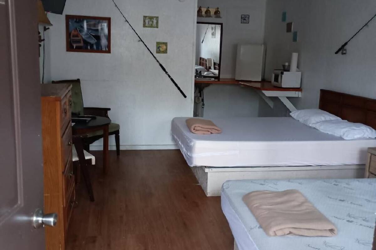 A bedroom with two beds, a desk, a chair, a ceiling fan, and a mirror.