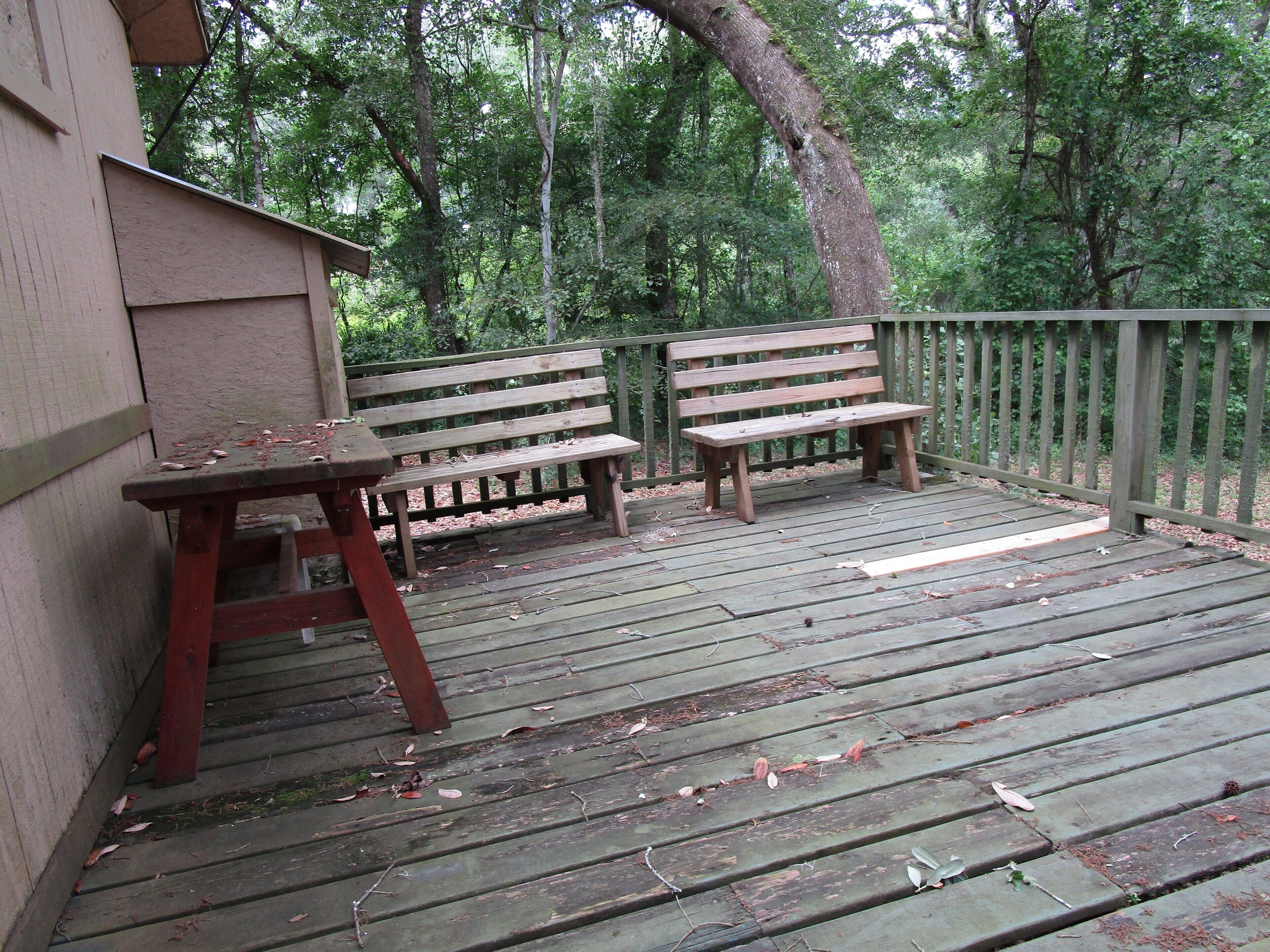 A wooden deck with two benches and a table, surrounded by a wooden fence and trees.