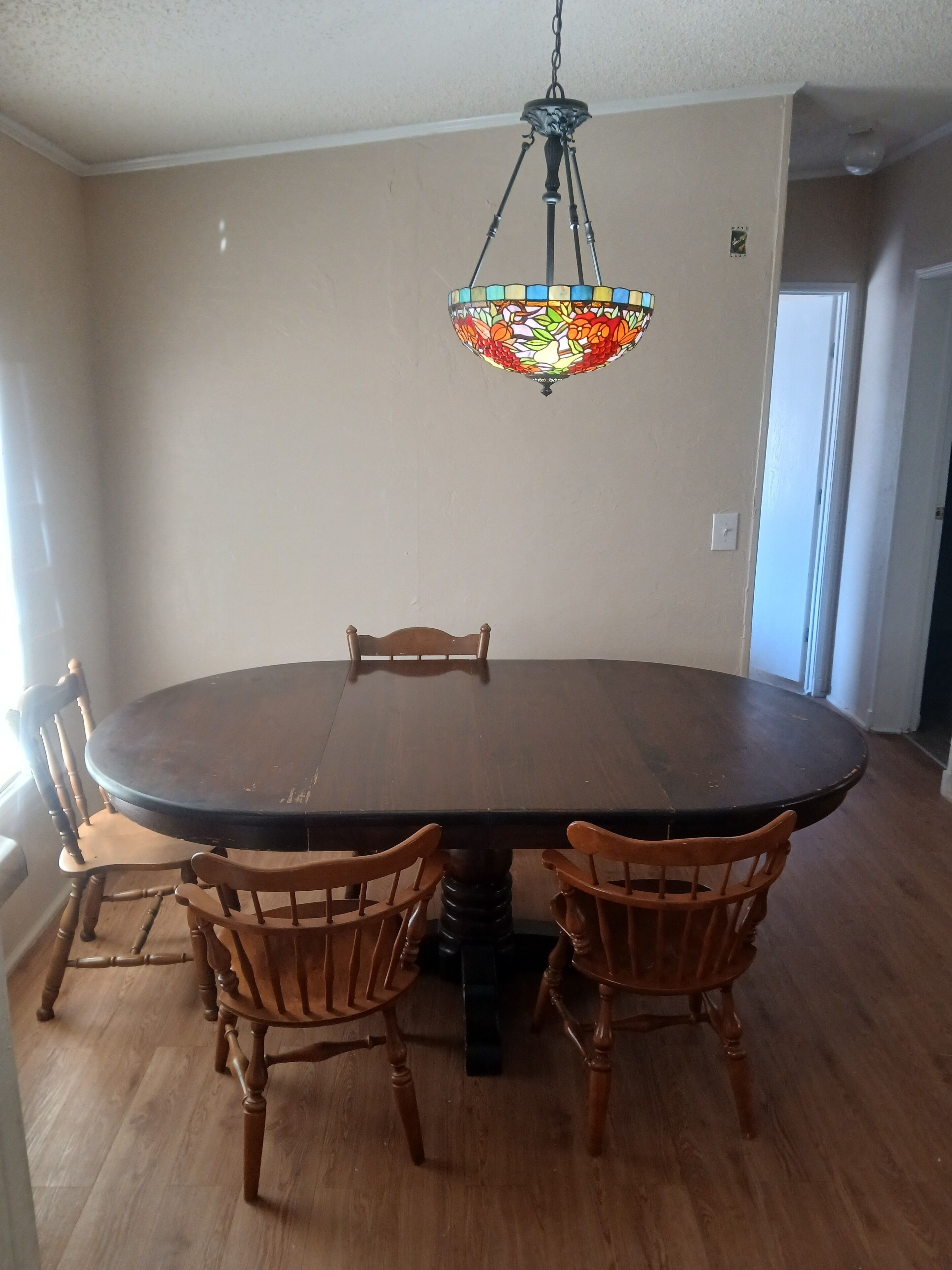 A dining area with a round table, four wooden chairs, and a stained glass chandelier.