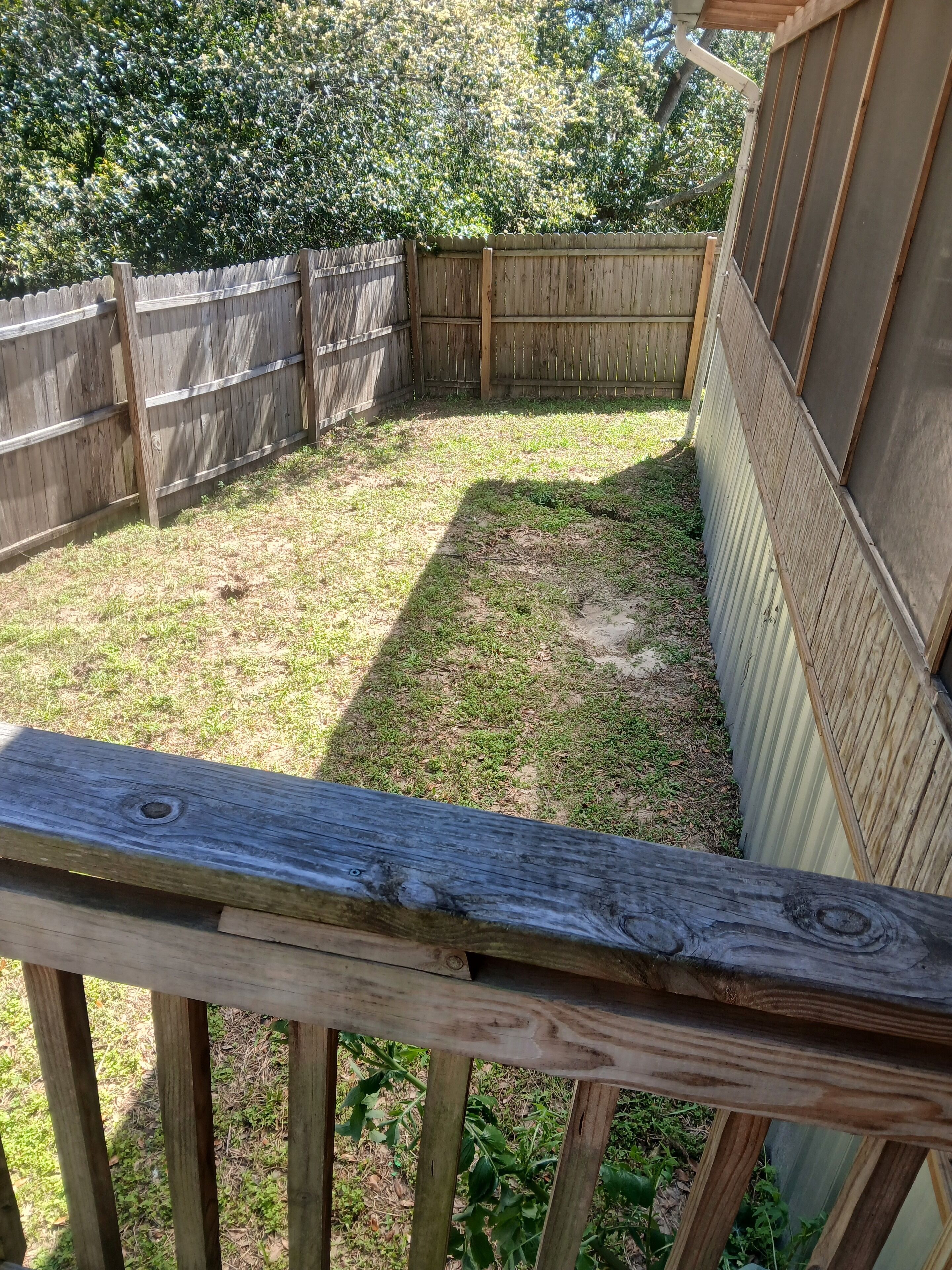 A wooden deck with a metal railing, a fenced backyard, and a corrugated metal wall.