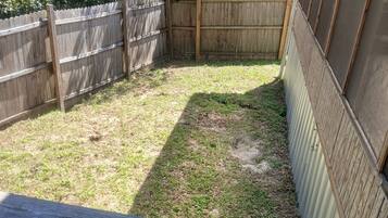 A wooden deck with a metal railing, a fenced backyard, and a corrugated metal wall.