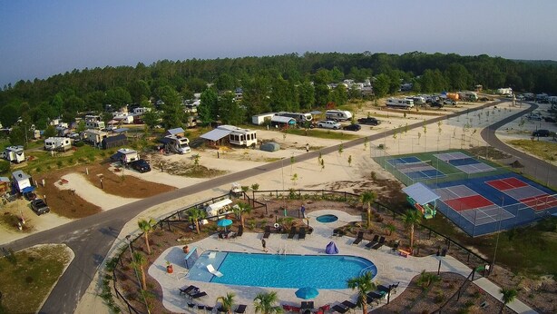Vista aérea de un camping con vehículos recreativos, piscina y canchas de tenis.