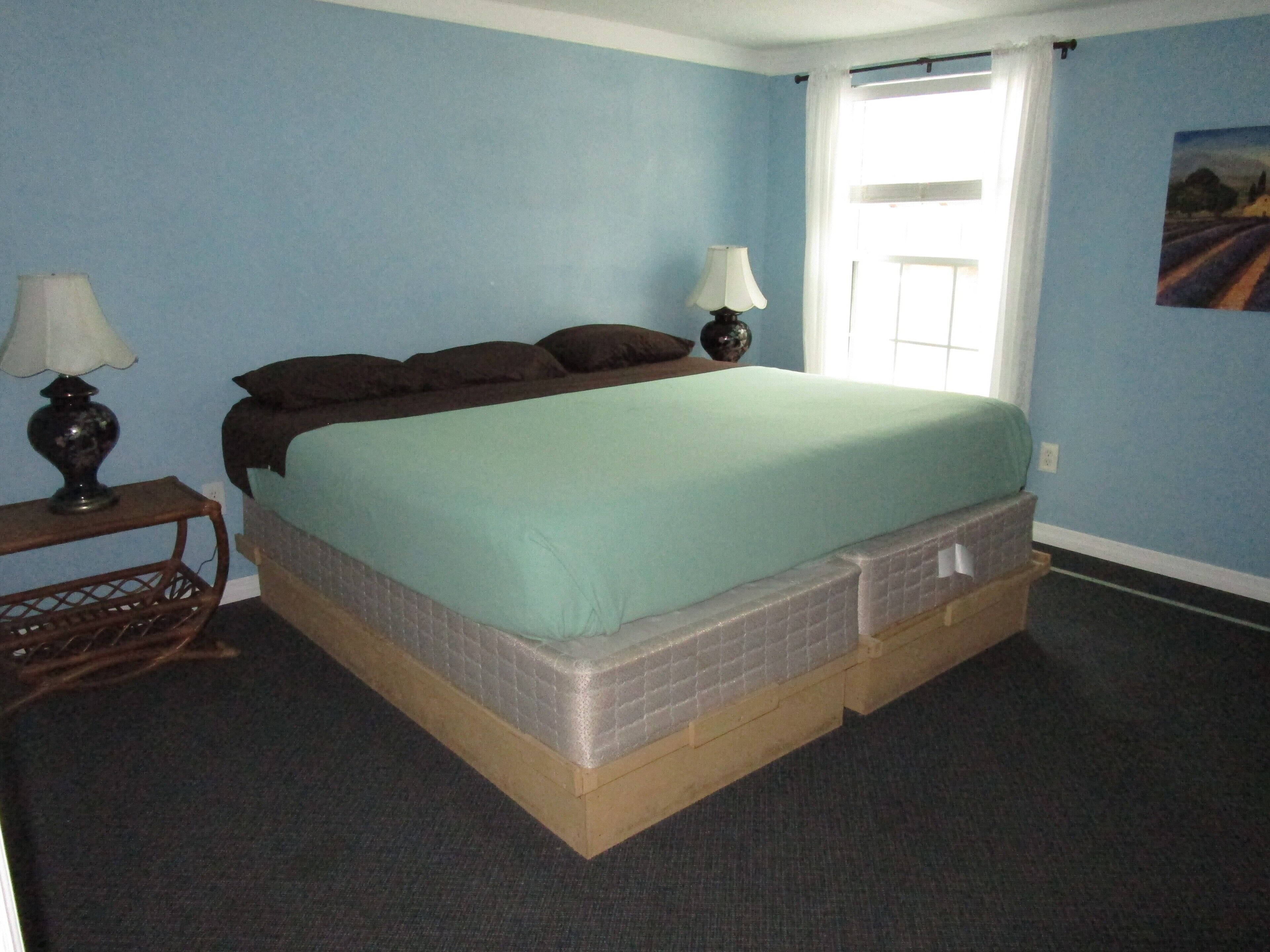 Un dormitorio con una cama, dos lámparas de noche, una mesita y una ventana con cortinas.