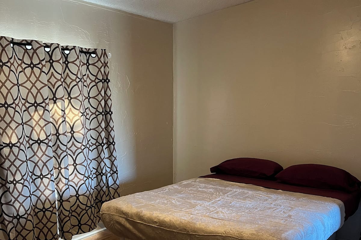 A bedroom with a bed, a ceiling fan, and a patterned curtain.