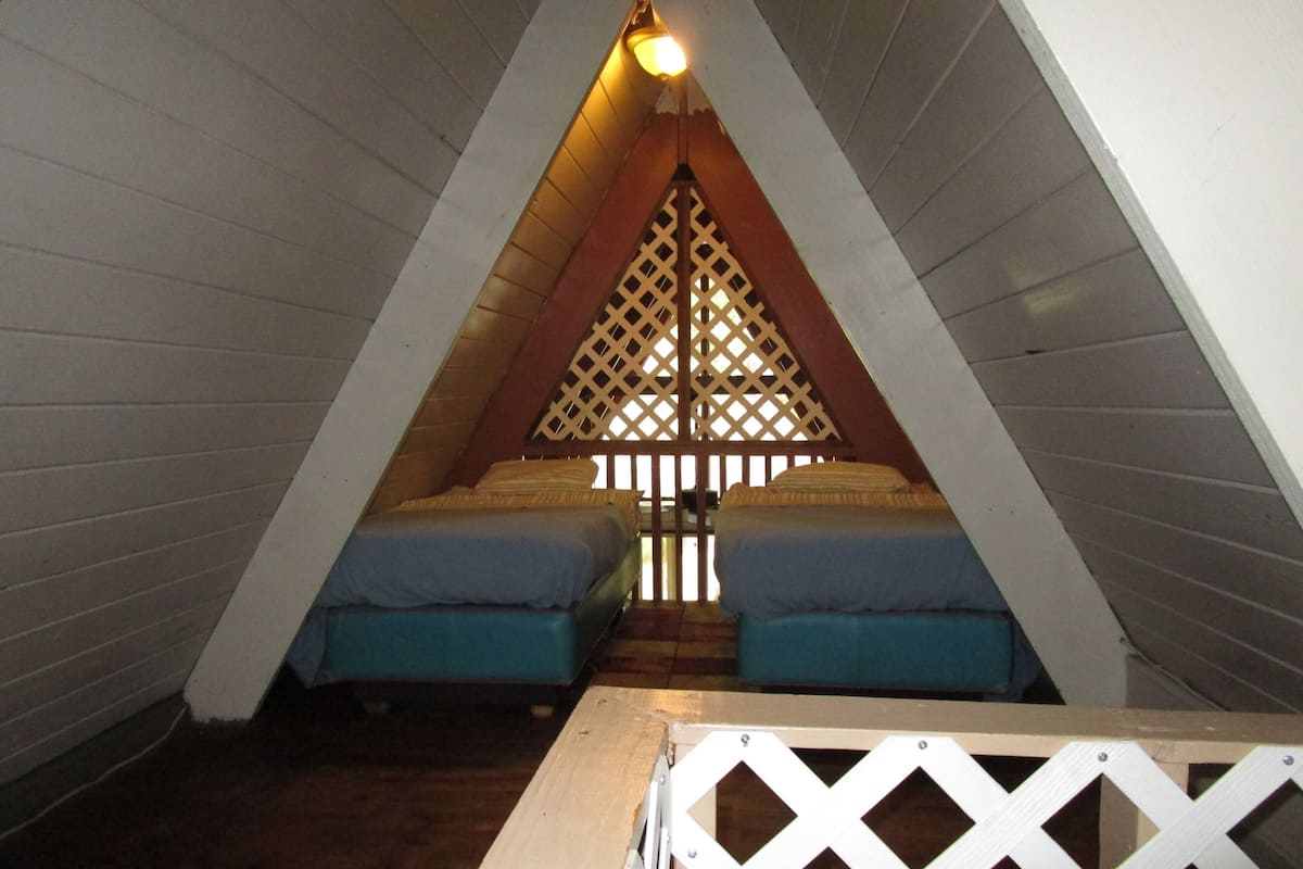 A small, triangular attic bedroom with two beds, wooden walls, and a lattice partition.