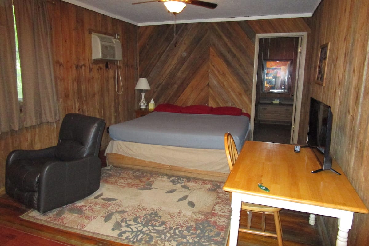 A room with a bed, a desk, a chair, a ceiling fan, and a television.