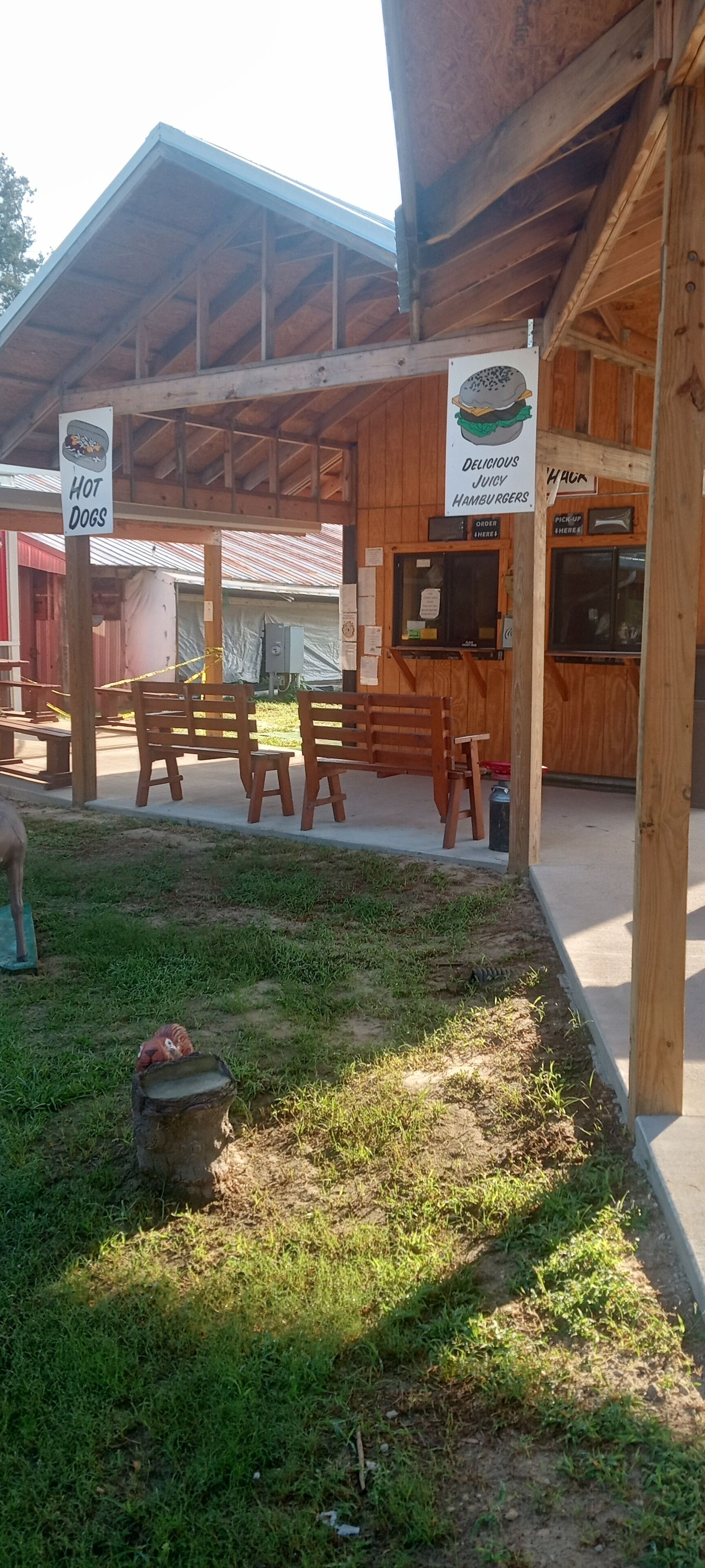 An outdoor seating area with wooden tables and chairs, a sign for 'Hot Dogs', and another sign advertising 'Delicious Juicy Hamburgers'.