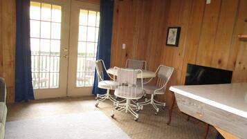 A room with a wooden paneled wall, a white table with four chairs, a door with a window, and a blue curtain.