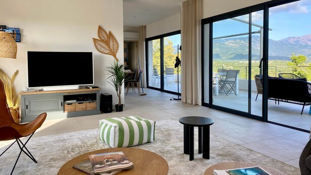 Amplia sala de estar con televisor grande, comedor y balcón con vista a la montaña.