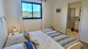 Un dormitorio con cama, lámpara de noche, ventana con vistas a montañas y baño con ducha.