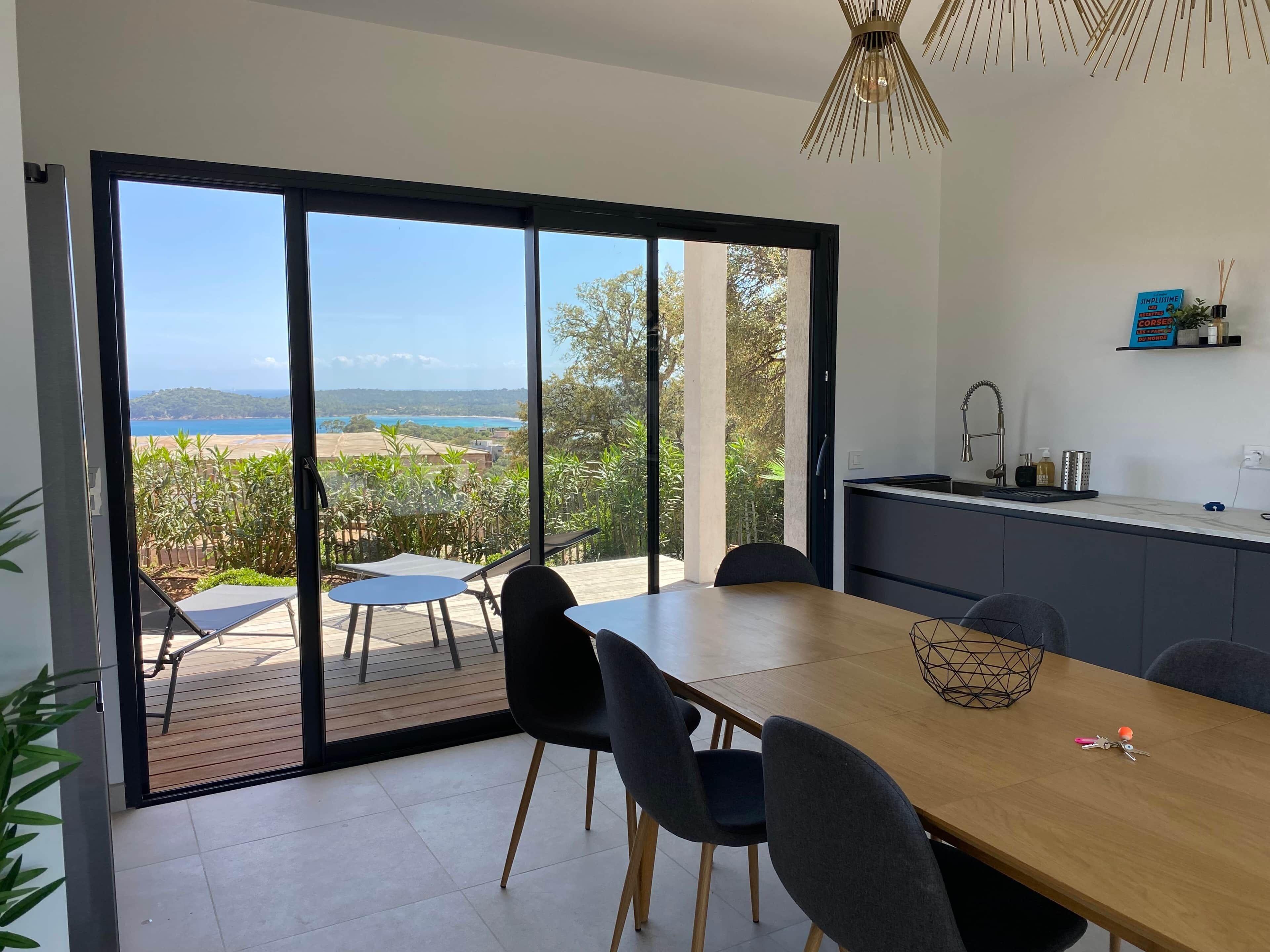 A modern dining area with a view of a coastal landscape, a kitchen with a sink and countertop, and a ceiling light fixture.