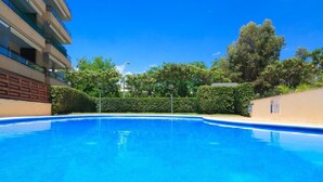 Una piscina con agua azul cristalina, rodeada de setos y árboles.
