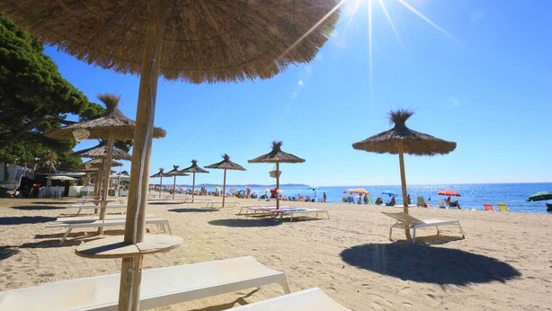 Una playa con sombrillas de paja y sillas reclinables blancas.