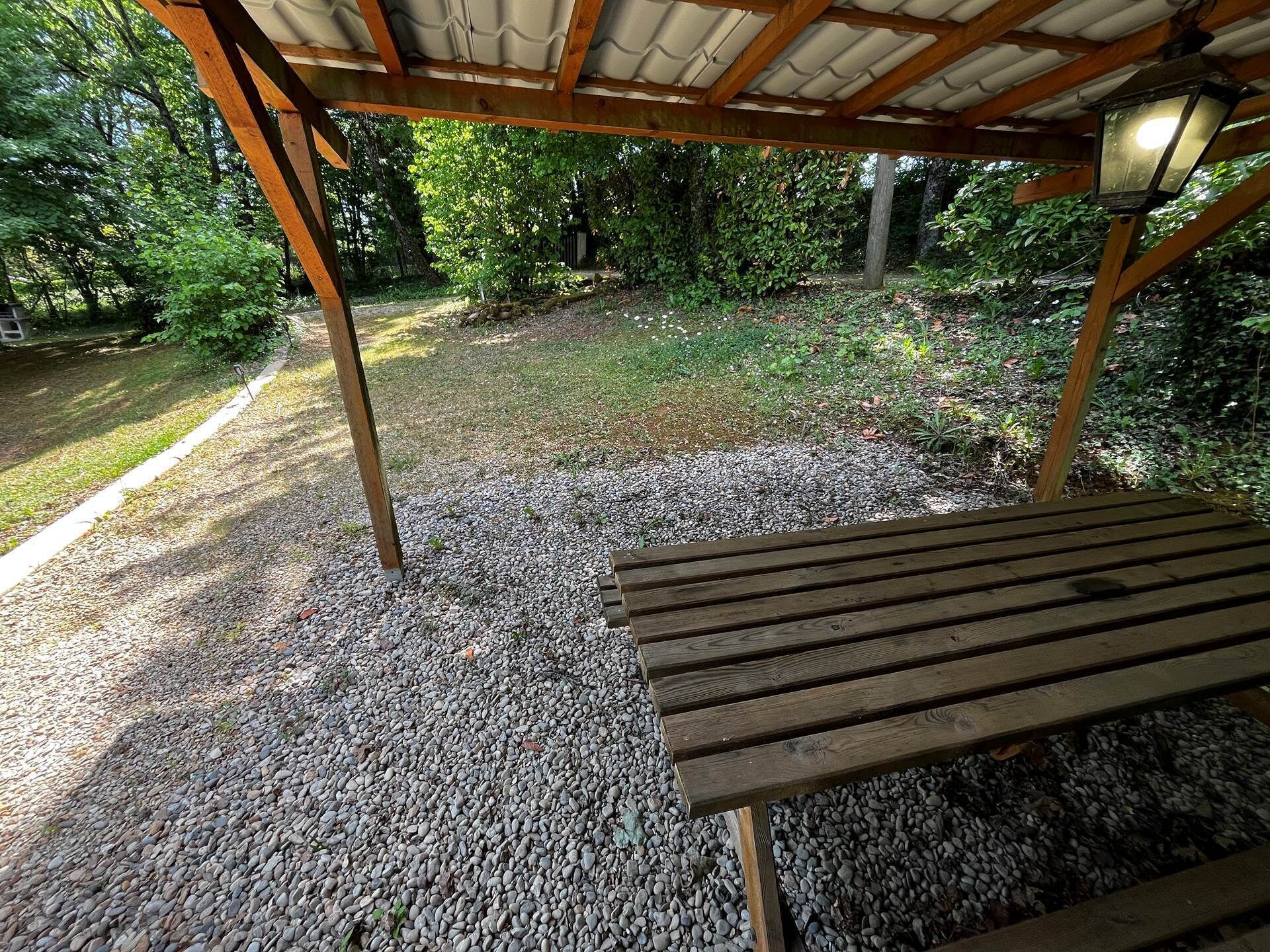 A wooden bench under a covered area with a gravel path leading to a grassy area.