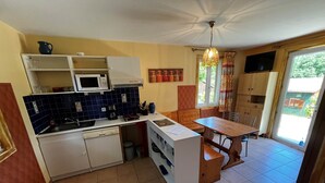 Une cuisine compacte équipée d’un four à micro-ondes, d’une cuisinière et d’un évier, ainsi qu’une table à manger en bois et une vue sur l’extérieur grâce à une porte-fenêtre coulissante.