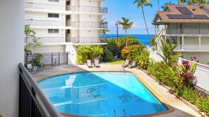 Une piscine avec vue sur l’océan, entourée de palmiers et bordée d’un bâtiment blanc doté de balcons.